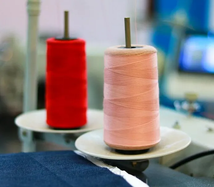 Close-up of red and pink thread spools on industrial textile machinery, highlighting the advanced manufacturing capabilities of Square Corporation's textile division.