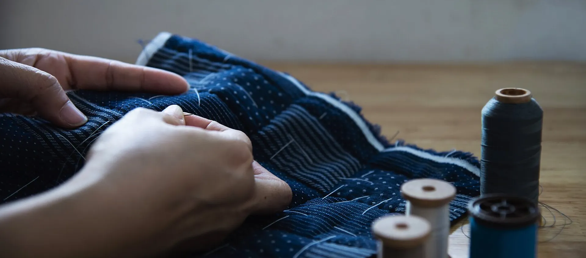 Detailed view of hands carefully stitching blue quilted fabric, showcasing the precision and craftsmanship within the textile and apparel business vertical.